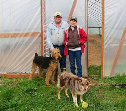 farmer Pat and his wife and dogs standing in front of a greenhouse