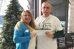 Happy female presents check to male director of food bank in front of christmas tree