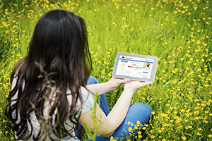 girl sitting in field of grass and flowers and holding tablet