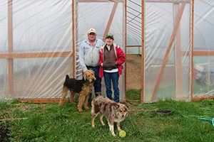 farmer Pat and his wife and dogs standing in front of a greenhouse