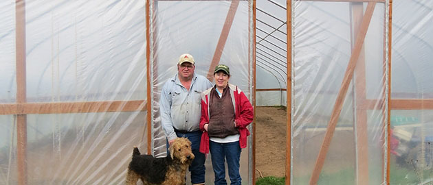 farmer Pat and his wife and dogs standing in front of a greenhouse