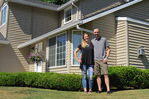 young couple standing on front lawn with their new house behind them.