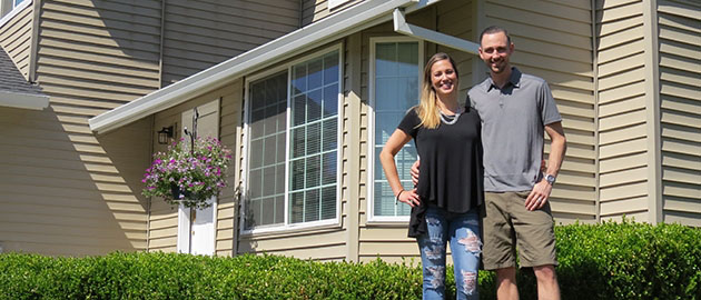 young couple standing on front lawn with their new house behind them.