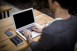 man sitting at table with laptop and phone