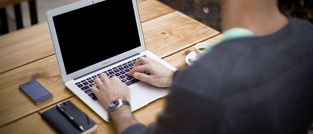 man sitting at table with laptop, phone and cup of coffee