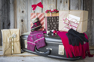 horizontal Christmas image of scarf and mitts along with gifts lying on a black suitcase all ready and packed to go on a Christmas vacation.