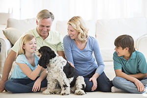 Happy little girl playing with dog while family looking at her in living room