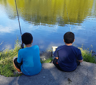 two boys with their backs to the camera holding fishing poles and fishing in a lake