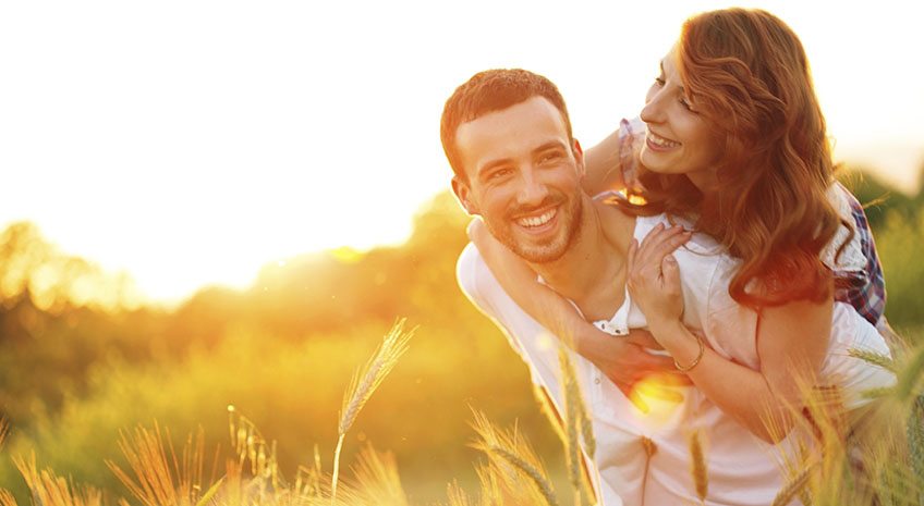 man carrying woman on his back while walking through wheat field