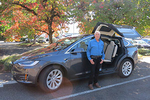 White haired mature man standing in front of dark grey SUV