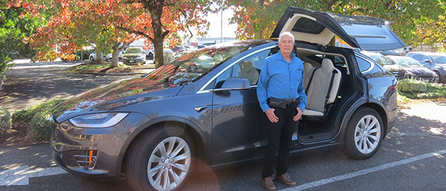 White haired mature man standing in front of dark grey SUV