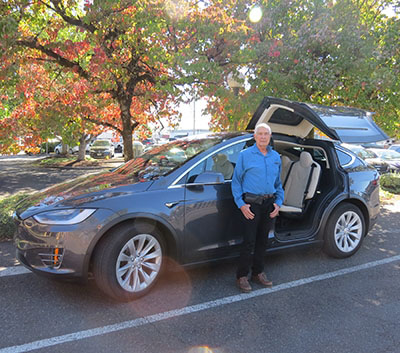 White haired mature man standing in front of dark grey SUV