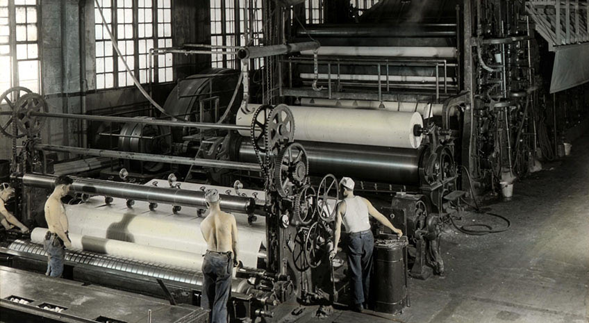 historical black and white photo of three men wearing jeans working at an industrial paper press
