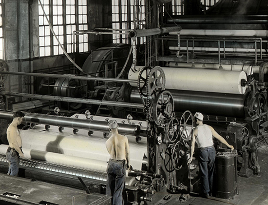historical black and white photo of three men wearing jeans working at an industrial paper press