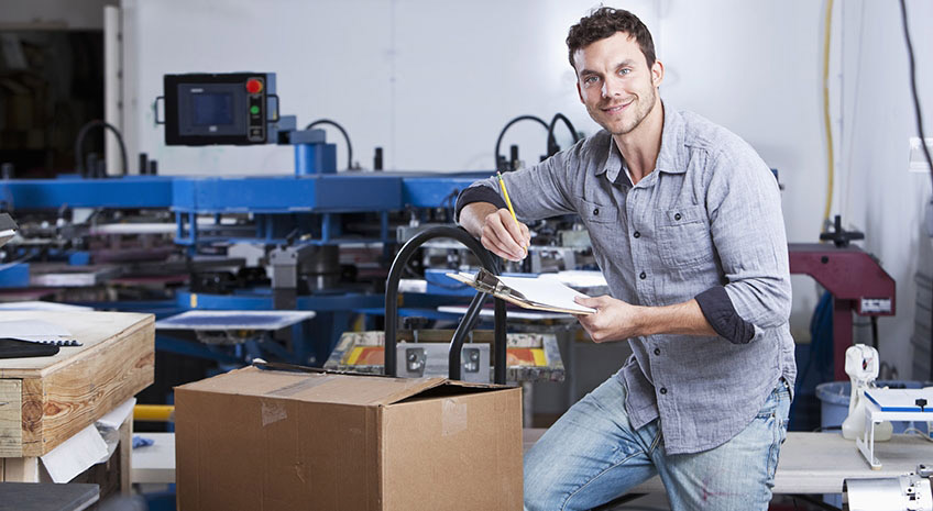 Small business - young man (20s) in screen printing factory with boxes ready for shipping.