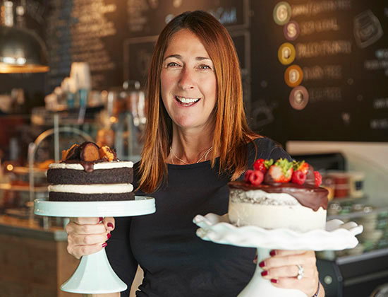 Portrait Of Female Owner With Cakes On Stands In Coffee Shop