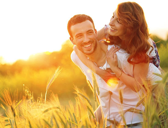 man carrying woman on his back while walking through wheat field