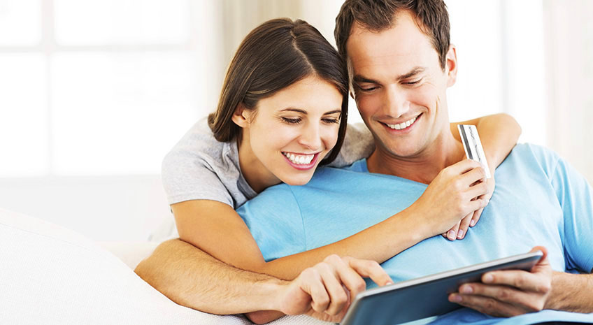 Happy loving couple using tablet computer and credit card at home. Horizontal shot.