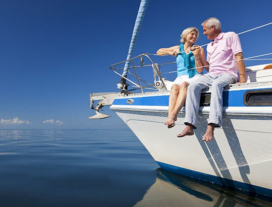 A happy senior couple sitting on the front of a sail boat on a calm blue sea