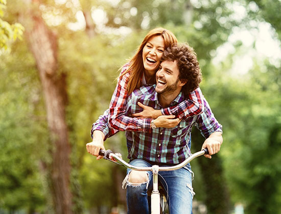 smiling and laughing man and woman riding together on bicycle through sunny wooded area