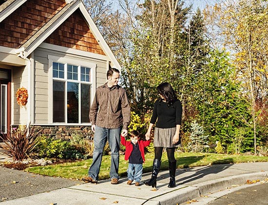 man and woman holding hands of small child while walking down a residential sidewalk