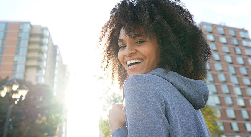 african american woman with curly hair smiling outside two tall buildings