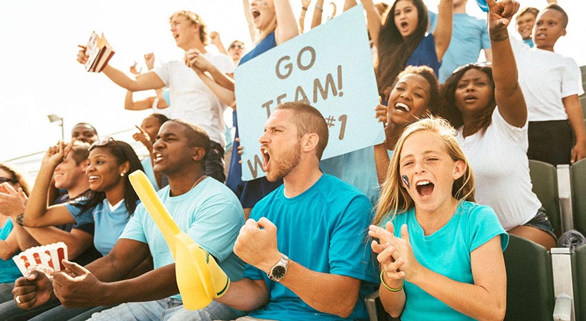 Excited crowd of fans cheering on team from stadium bleachers