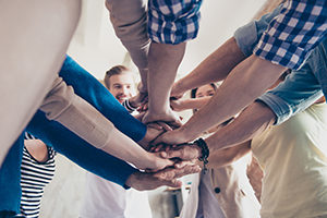 Low angle cropped view of colleagues putting their hands on top of each other, wearing casual clothes. Concept of successful teambuilding and unity