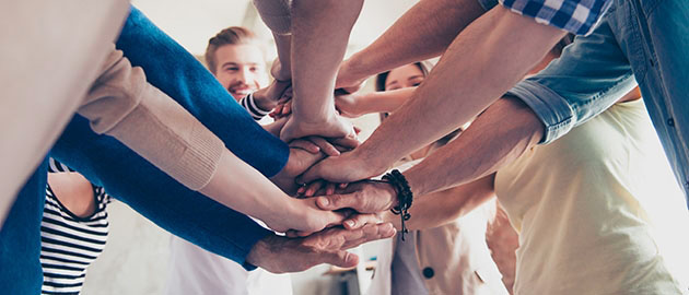 Low angle cropped view of colleagues putting their hands on top of each other, wearing casual clothes. Concept of successful teambuilding and unity