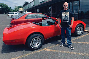 mature man standing next to classic red convertible corvette