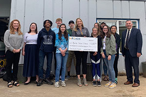 President/CEO Brooke Van Vleet holding large novelty check surrounded by a diverse group of students and teachers