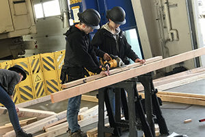 group of high school students in black hard hats cutting lumber with a power tool