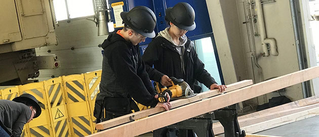 group of high school students in black hard hats cutting lumber with a power tool