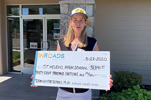 Middle aged woman with blonde hair wearing a baseball cap and holding an oversize check made out to St. Helens High School