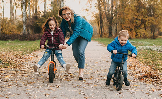 Smiling caucasian mother is playing with her small kids while teaching them to ride the bike