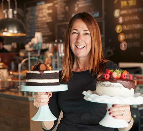 women in cafe holding cakes on stands