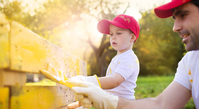 son and dad in red hats painting a fence