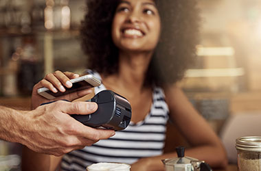 Shot of a beautiful woman using her smart phone and an electronic reader to pay her bill in a coffee shop