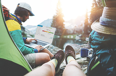 Young active couple hiking together in stunning mountain wilderness near the lake. POV from the tent. Woman sitting inside, man wearing backpack and using laptop in the wild, good network coverage