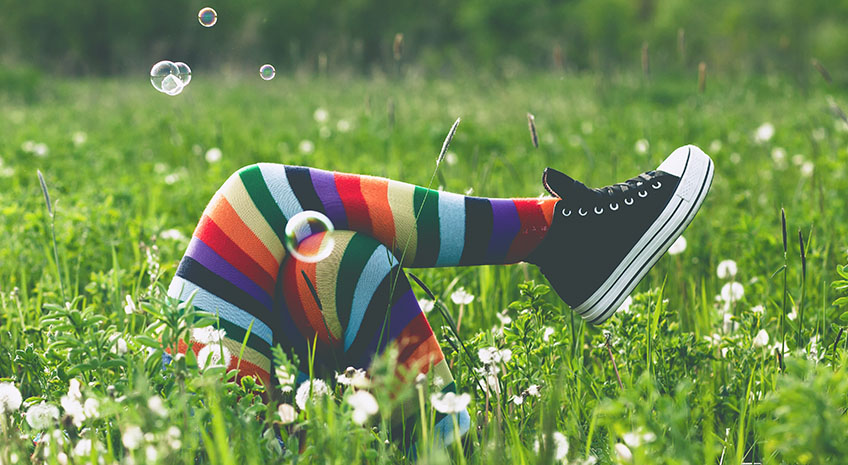 rainbow socks and black sneakers on an unseen person's legs lying in the grass