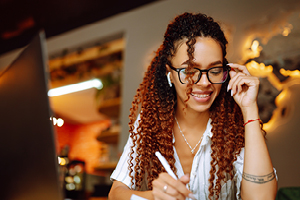 Portrait of African American woman sitting at cafe having video call on laptop computer. Woman, student wearing headphones calling on laptop, talk by webcam with friend or relative, online course.