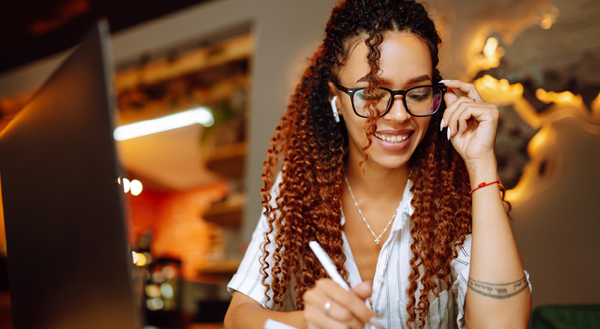 Portrait of African American woman sitting at cafe having video call on laptop computer. Woman, student wearing headphones calling on laptop, talk by webcam with friend or relative, online course.