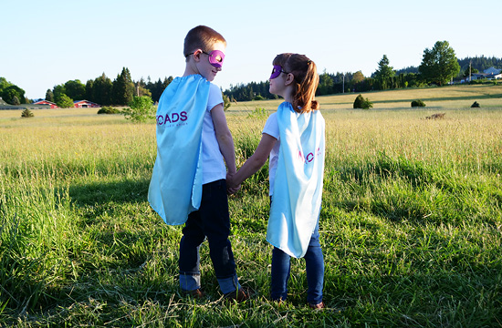 two kids in a field with capes and masks