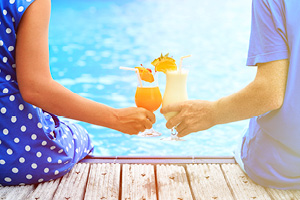 2 people sitting on a dock, toasting fancy drinks in the sunshine