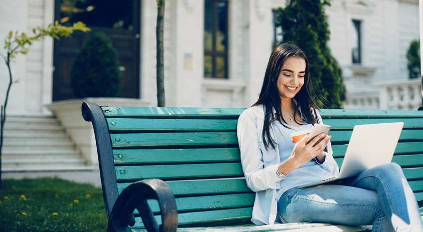 woman sitting on bench with cell phone and laptop