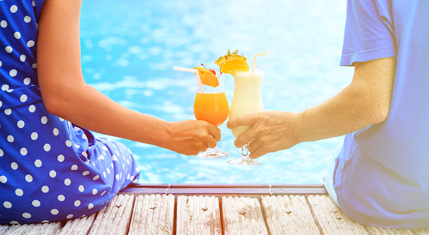 2 people sitting on a dock, toasting fancy drinks in the sunshine