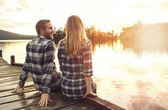 man and woman in flannel shirtd sitting on a lake dock looking at the sunset