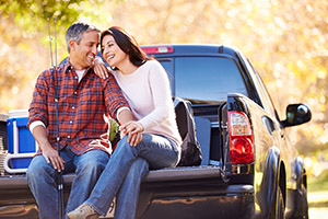 Couple Sitting In Pick Up Truck On Camping Holiday Smiling