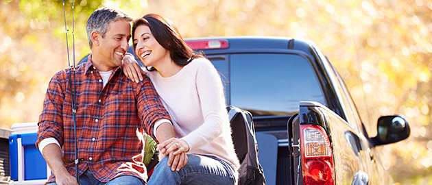 Couple Sitting In Pick Up Truck On Camping Holiday Smiling
