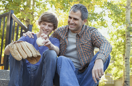 father and son sitting on porch smiling, son has a baseball and glove